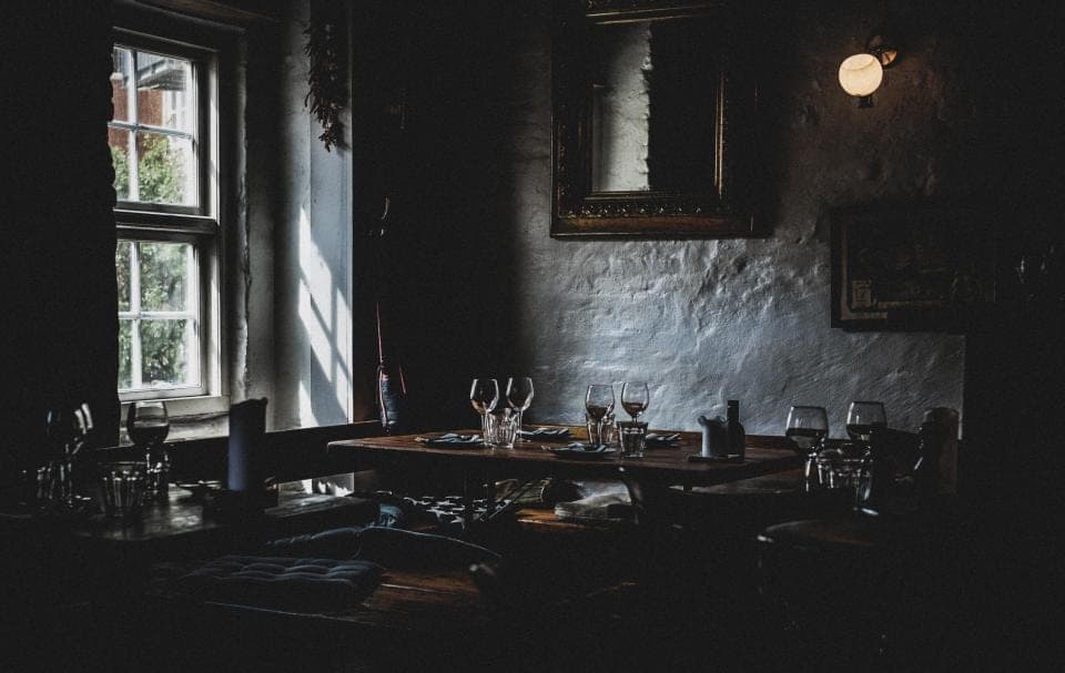 A dark dining room with set tables and whitewashed walls