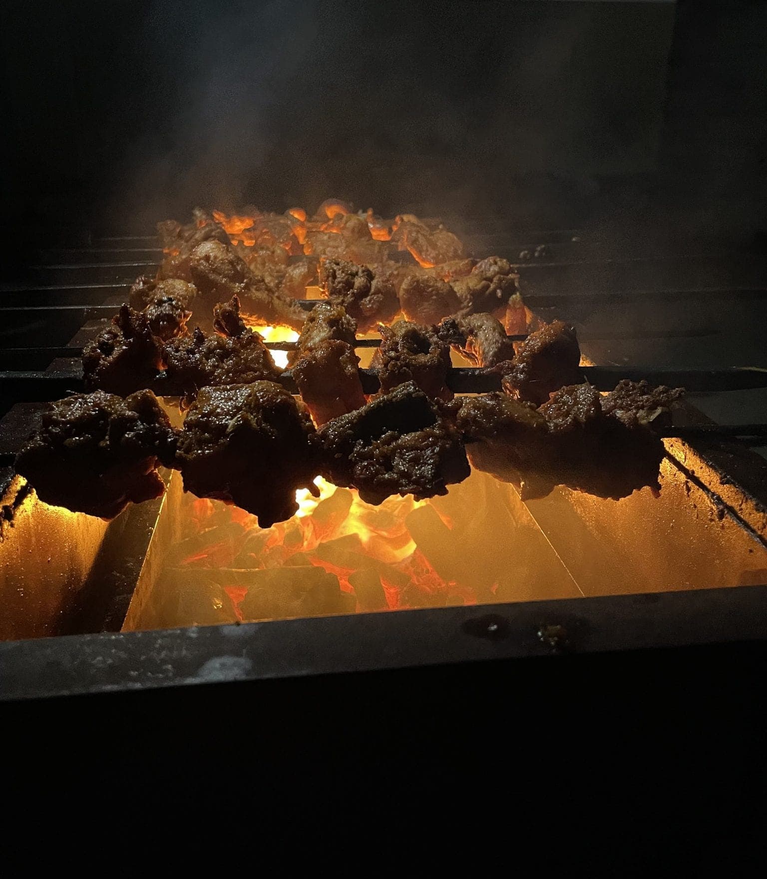 Skewers of meat over glowing charcoal on the grill